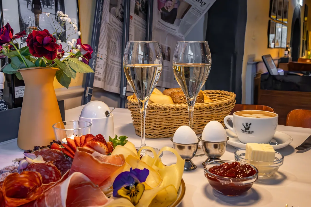 Breakfast table with cold cuts, cheese, eggs, bread basket, cappuccino and sparkling wine at Café Nüsslein Erfurt